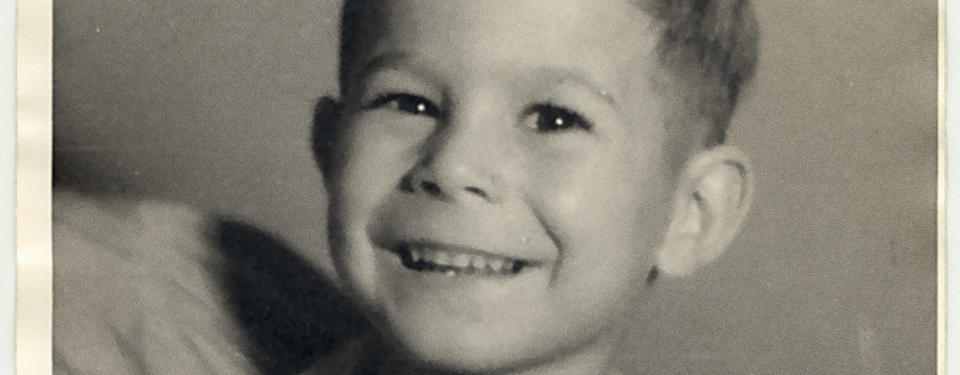 Bilden är en porträttbild tagen i fotostudio på en ung pojke som ler mot kameran.