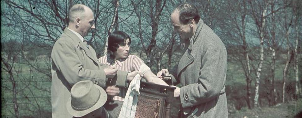 Bilden visar när rasbiologen Robert Ritter och en av hans assistenter tar blodprov på en ung tysk sintikvinna. Kvinnan sträcker fram armen. Provet tas utomhus.