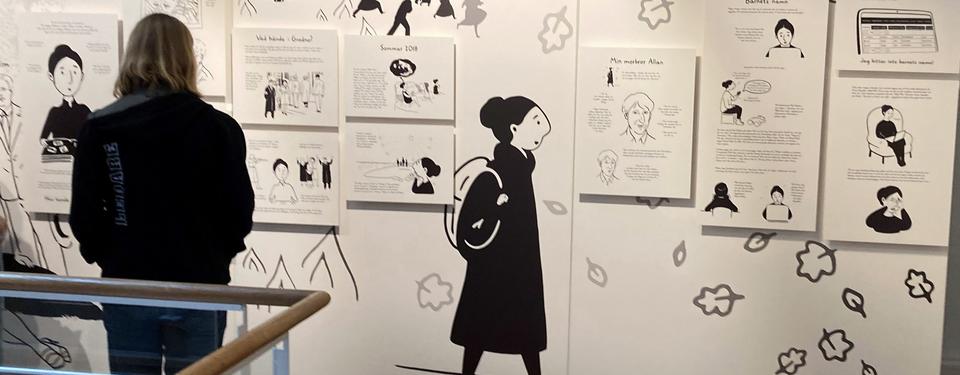 Bilden visar silhuetten av en person som står och tittar på en vägg med svartvita teckningar ur utställningen 