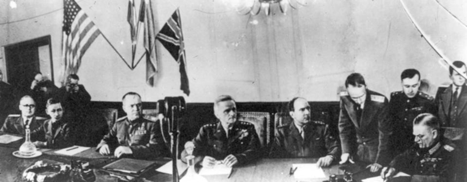 Bilden visar sex män sittandes framför dokument vid avlångt bord.