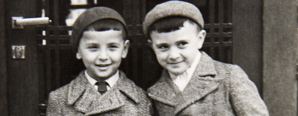 Bilden visar två leende pojkar i ytterplagg med kavajslag och basker.
