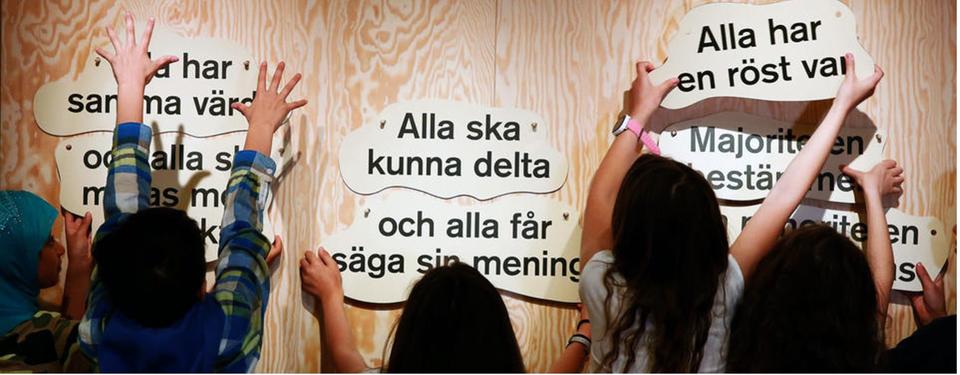Bilden visar barn som sätter upp lappar med text på en vägg