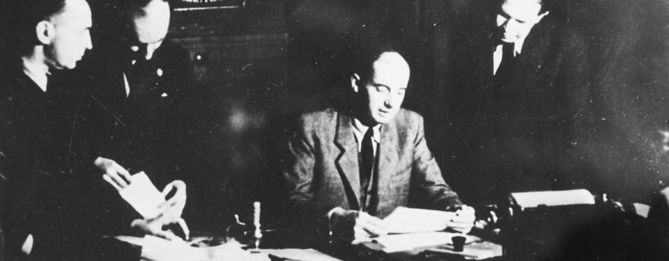 Bilden visar Raoul Wallenberg sittandes vid bord med dokument och tre män ståendes bakom.