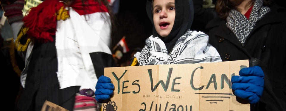 Bilden visar barn i en folksamling hållandes skylt med texten yes we can and we did 2/11/2011.