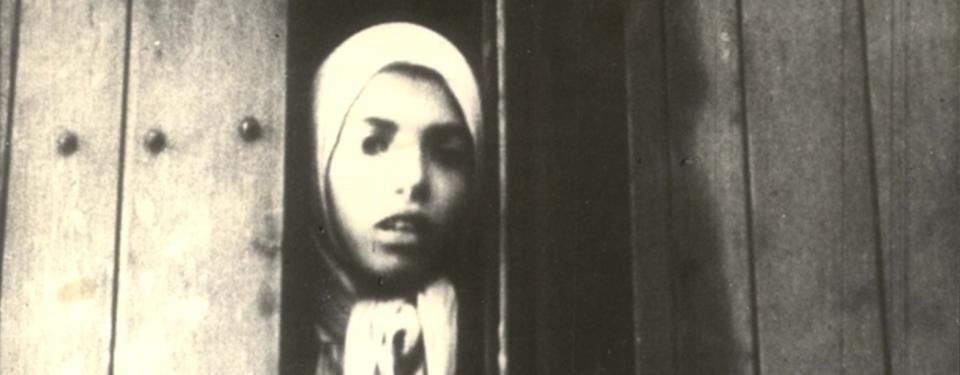 En svartvit bild på en flicka med sjalett som tittar ut från en tågvagn.