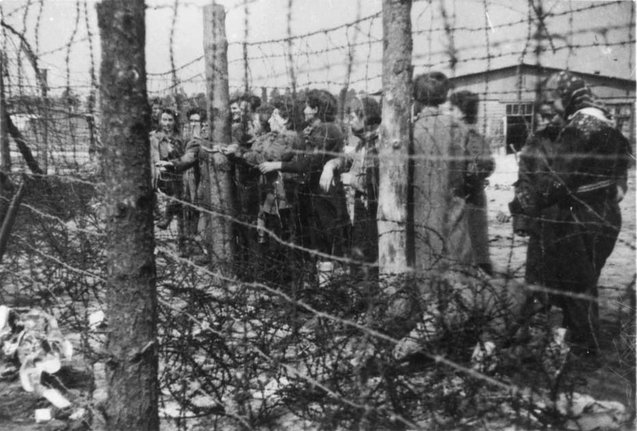 Bilden visar ett femtontal kvinnor ståendes nära taggtrådsstängsel.