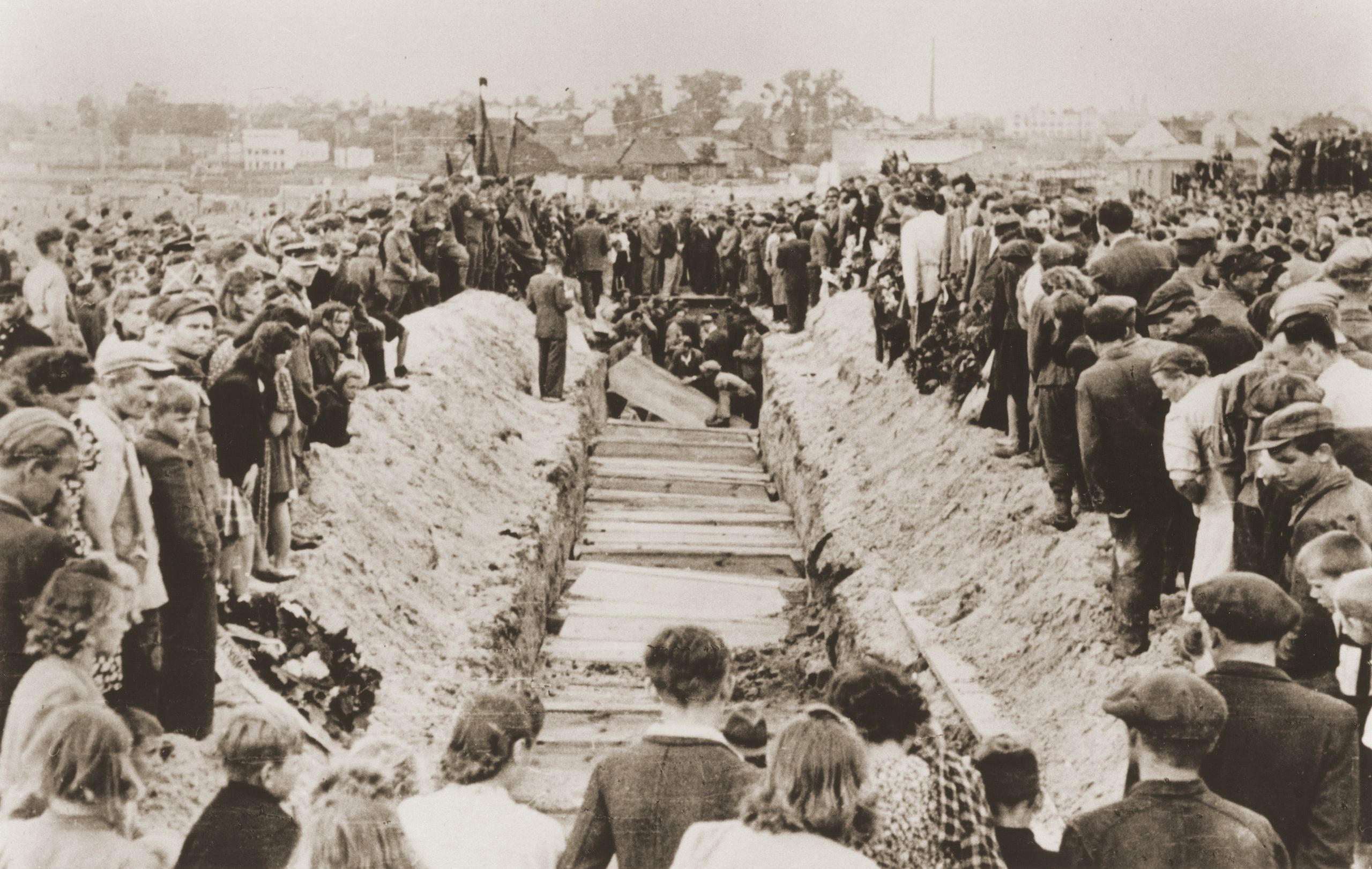 Bilden visar en lång rad av kistor omringad av en stor folkmassa.