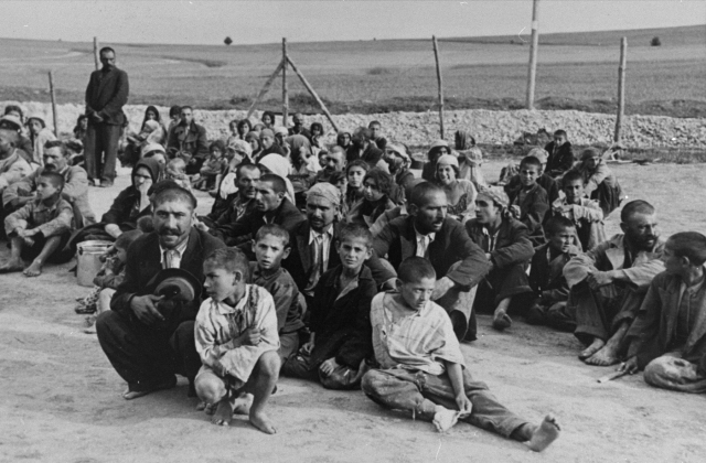 Bilden visar ett femtiotal män, kvinnor och barn sittandes på marken.