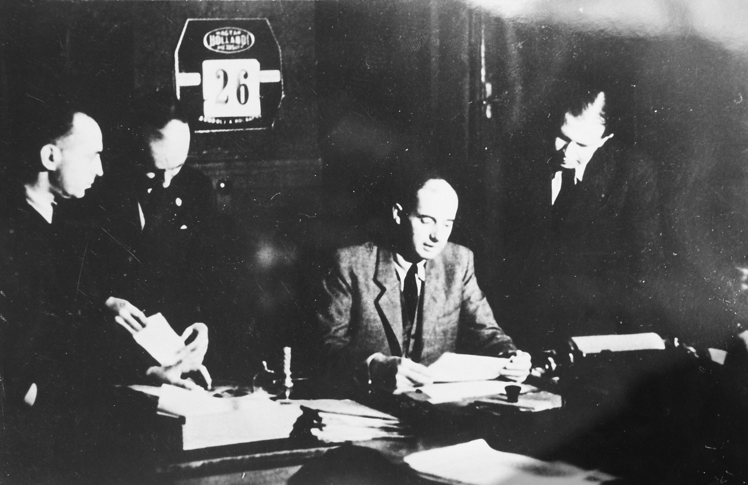 Bilden visar Raoul Wallenberg sittandes vid bord med dokument och tre män ståendes bakom.