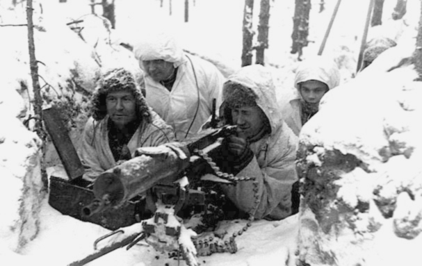 Bilden visar fyra män sittandes i skyttegrav vintertid. En man siktar med ett vapen.