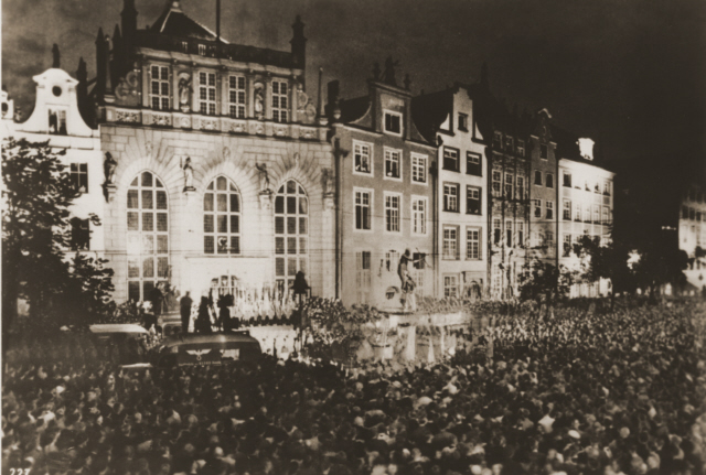 Bilden visar stor, tät folkmassa framför äldre byggnad.