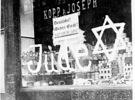 Bilden visar ett skyltfönster med texten jude samt en stjärna skrivet stort på fönstret.