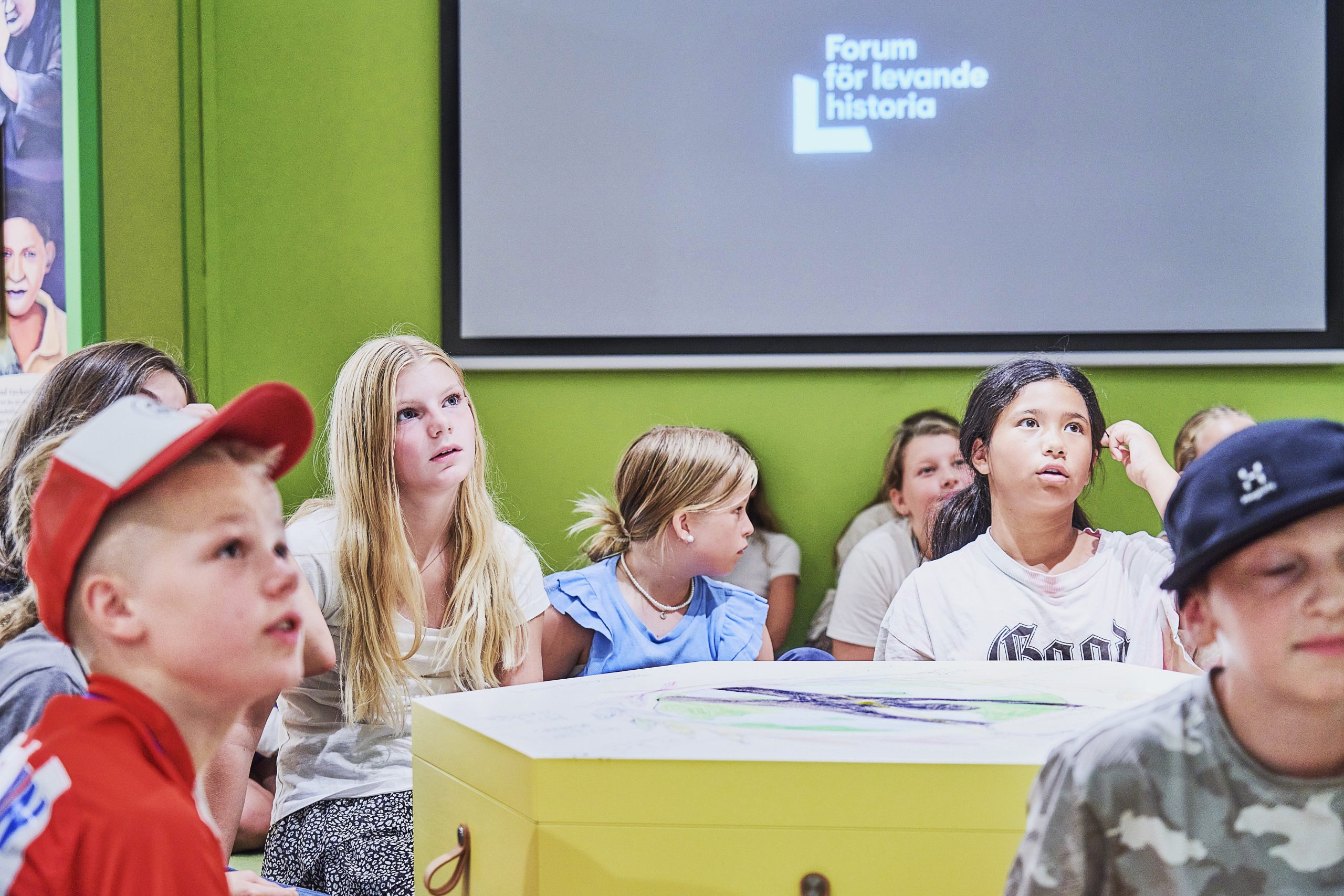 En grupp barn i en färgglad miljö tittar intresserad på något utanför bild.