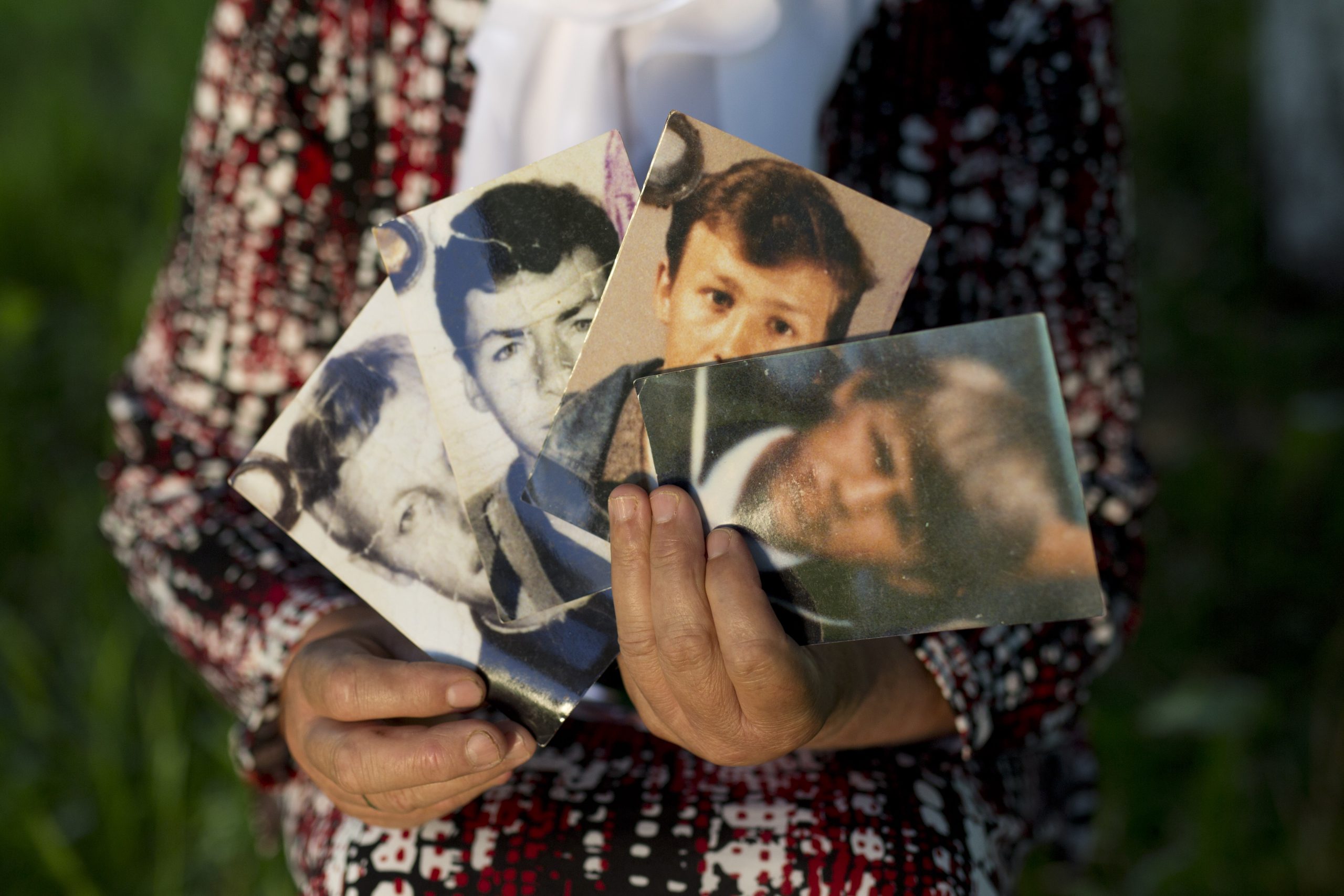 En kvinna håller upp fotografier av hennes man och söner.