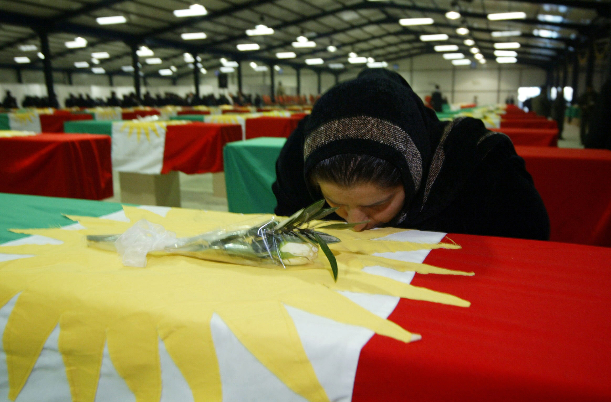 Bilden visar kvinna kyssandes flaggtäckt kista i ett stort rum med många flaggtäckta kistor.