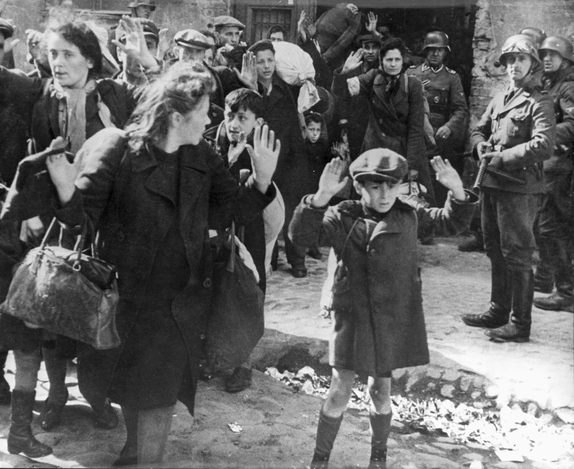 Bilden visar en pojke och en kvinna i närbild med händerna i luften och en soldat pekandes sitt vapen mot dem.