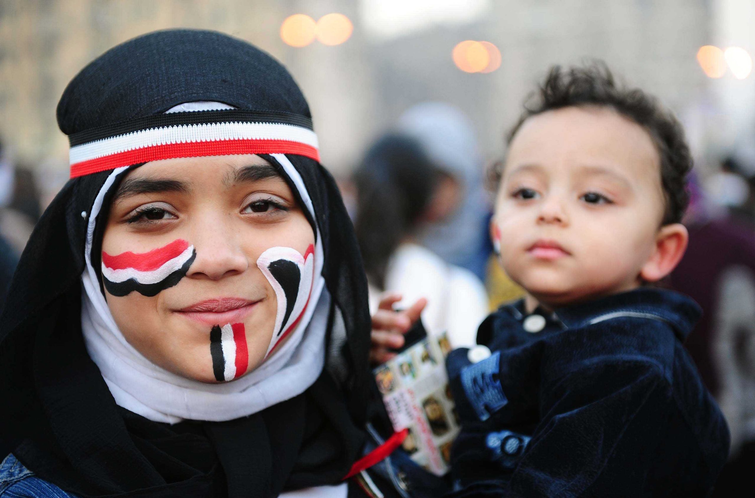 Bilden visar en kvinna som håller i sitt lilla barn. Kvinnan är målad i egyptens flaggas färger.