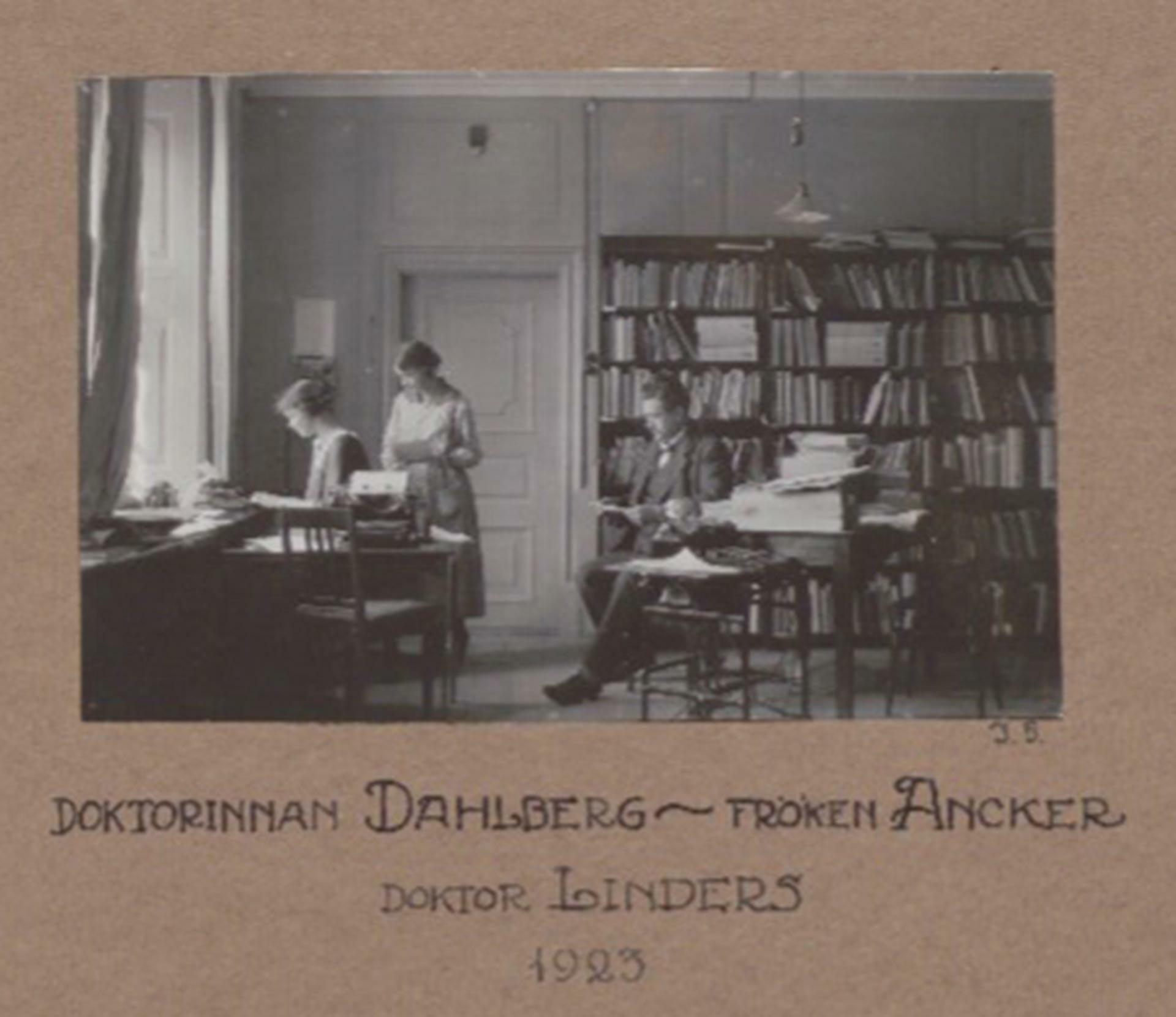 Tre personer i ett arbetsrum. Två kvinnor vid ett skrivbord och en man framför en bokhylla.