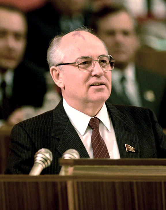 En man i 60-årsåldern, Michail Gorbatjov, med glasögon och grått hår står vid ett talarpodium med mikrofoner på.