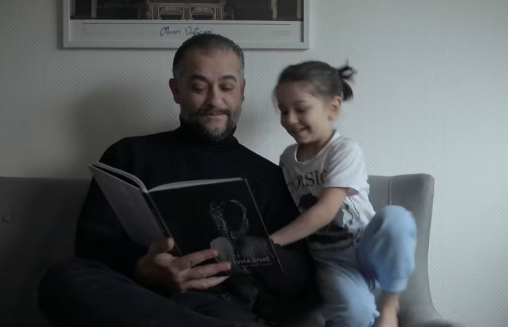 En pappa och ett barn tittar i en bok i en soffa.