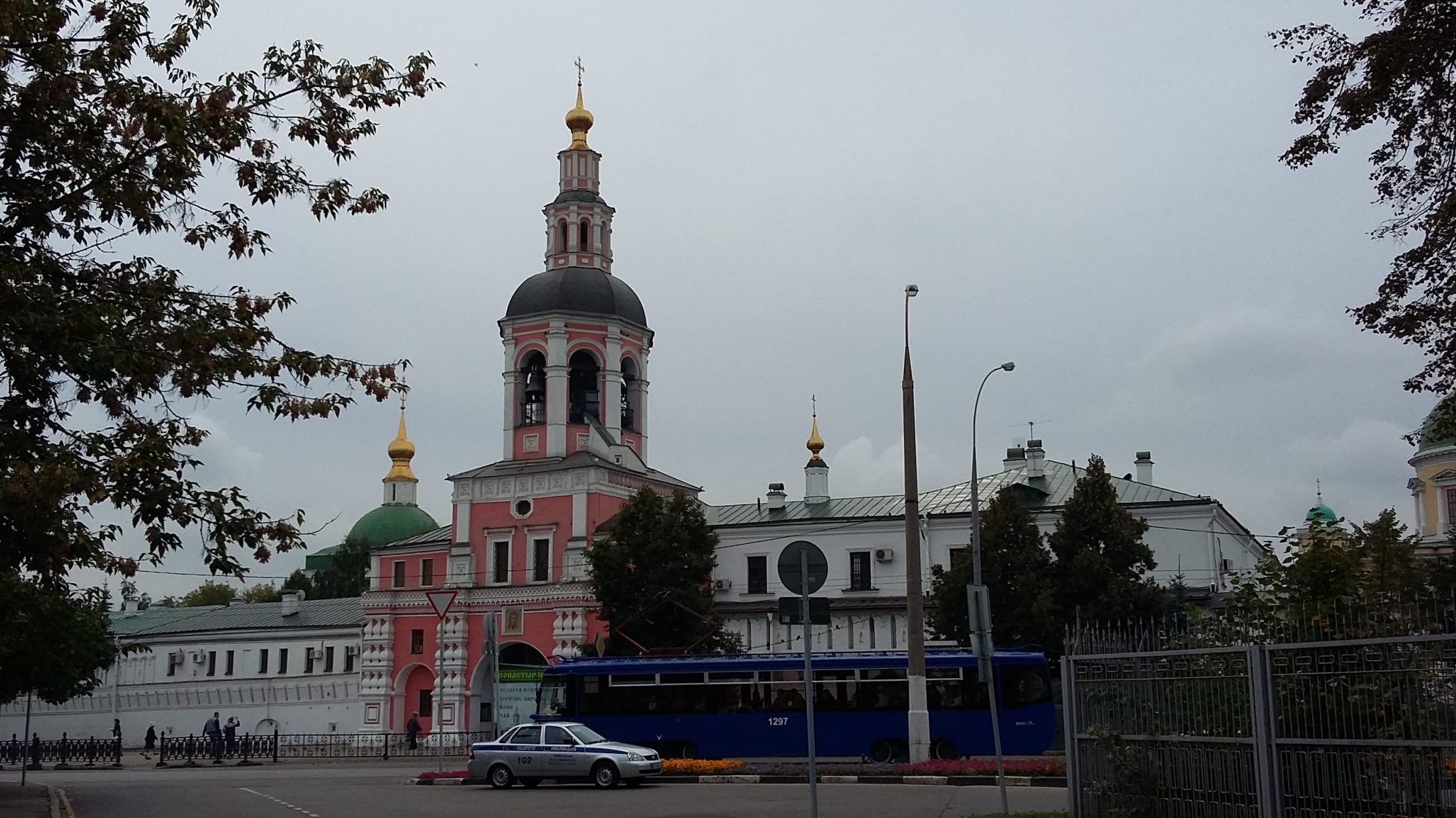 Ur en större vit byggnad reser sig ett högt rött torn med kupol och guldfärgad spira i toppen.