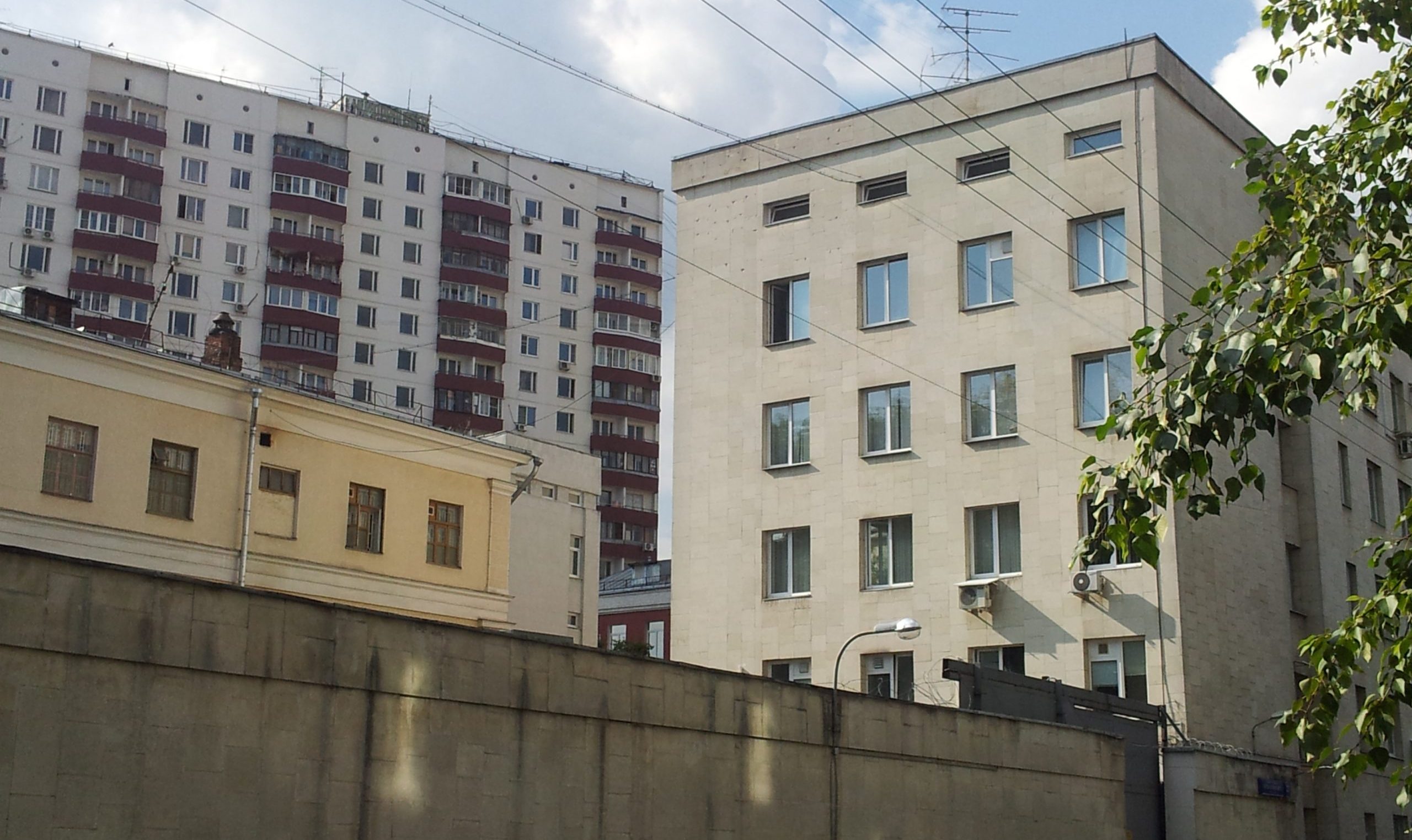 Bakom en hög betongmur skymtar en anonym grå byggnad i sex våningar.