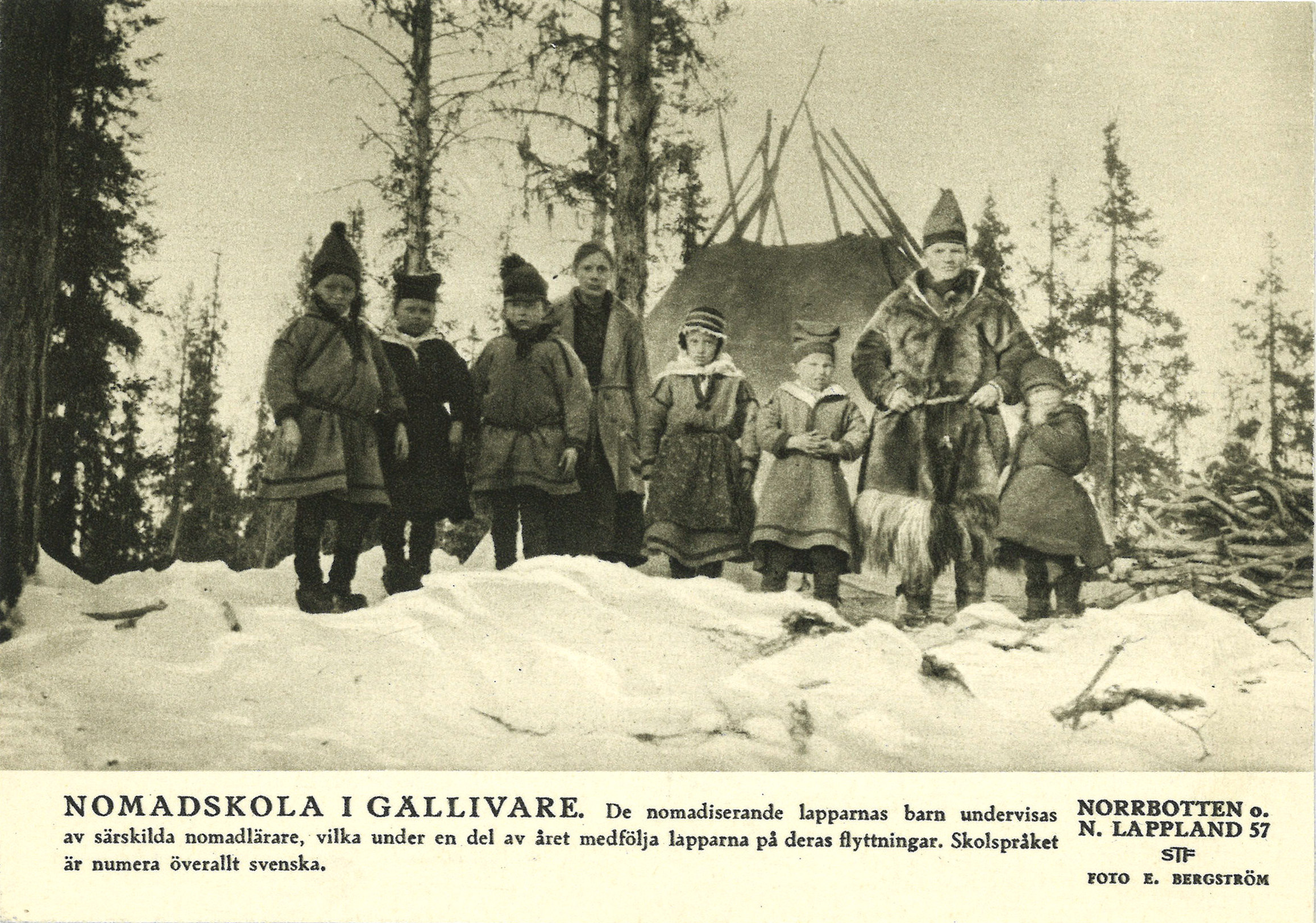 Svartvitt foto av barn som står uppradade utanför en kåta i en snötäckt skogsmiljö.
