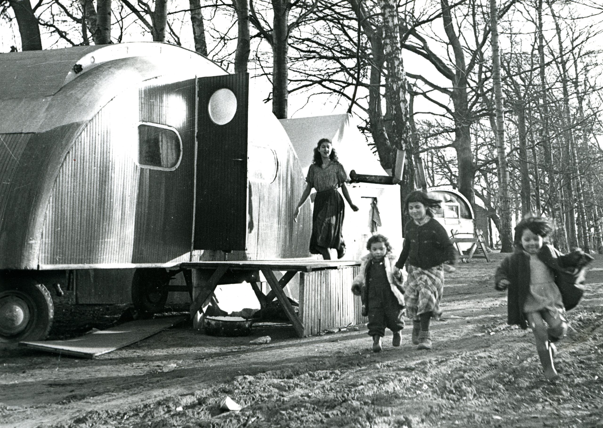 Svartvitt foto föreställande barn som leker framför en större husvagn.