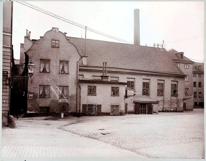 Äldre svartvitt foto föreställande ett stenhus i tre våningar.