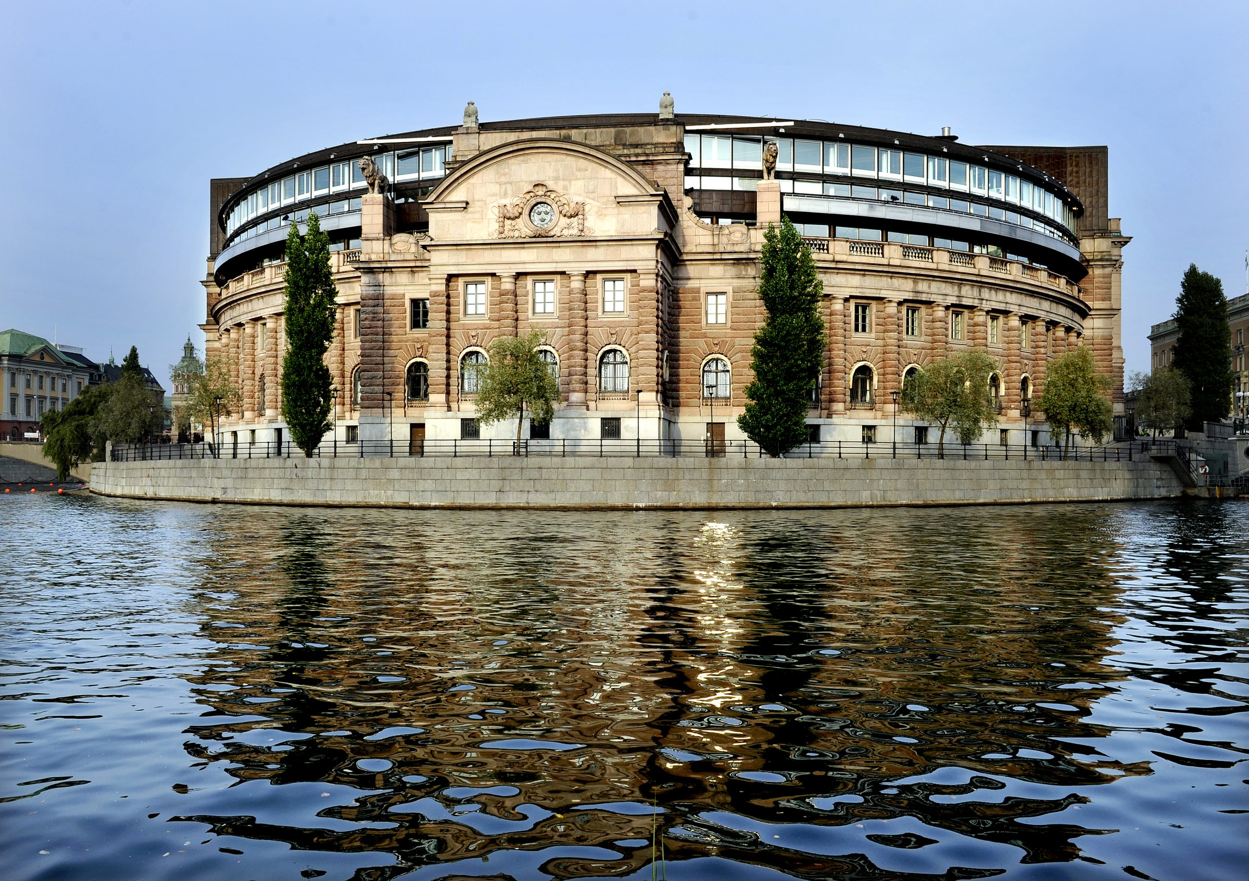 Sveriges riksdag med vatten i förgrunden. Det är en äldre och stor byggnad.
