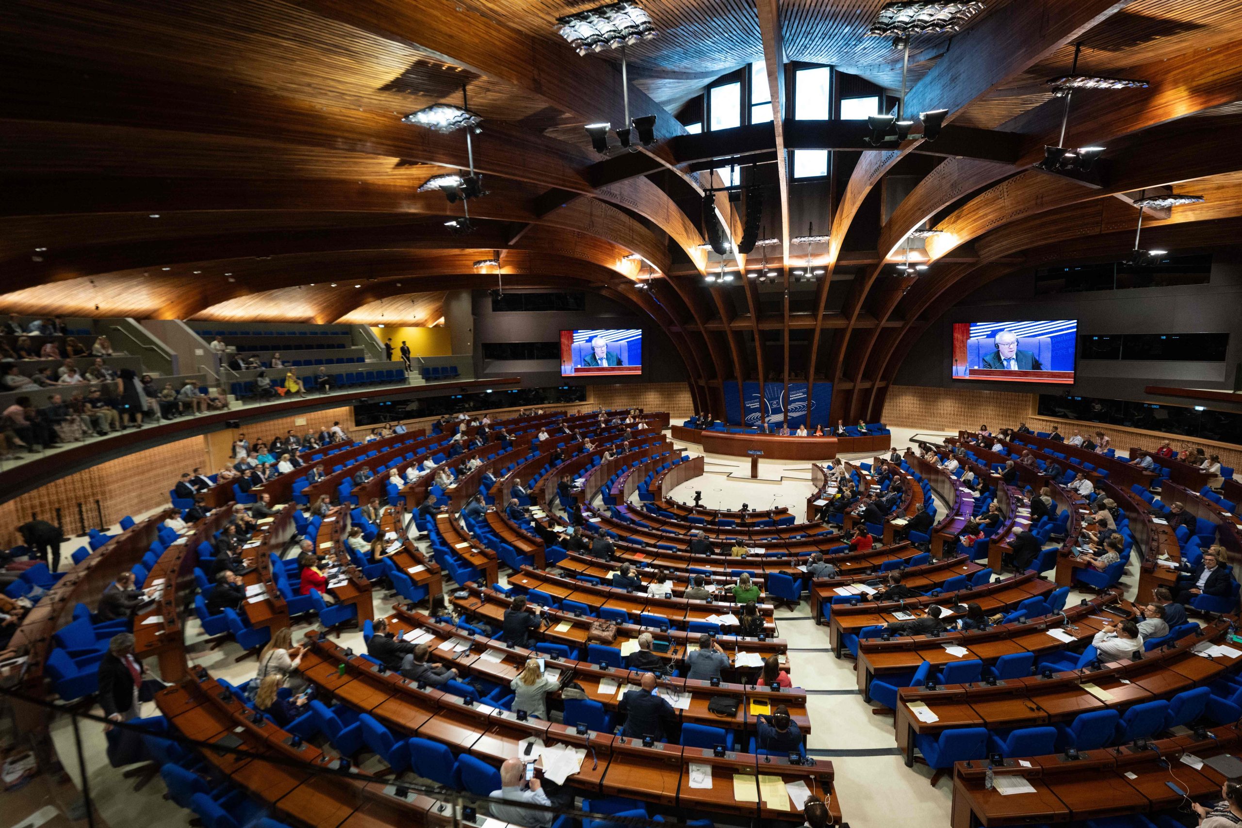En stor cirkelformad sal. Längst bort i bild syns en scen. I åhörarbänkar är möblerade i ett slag halvcirkelformation framför scenen.