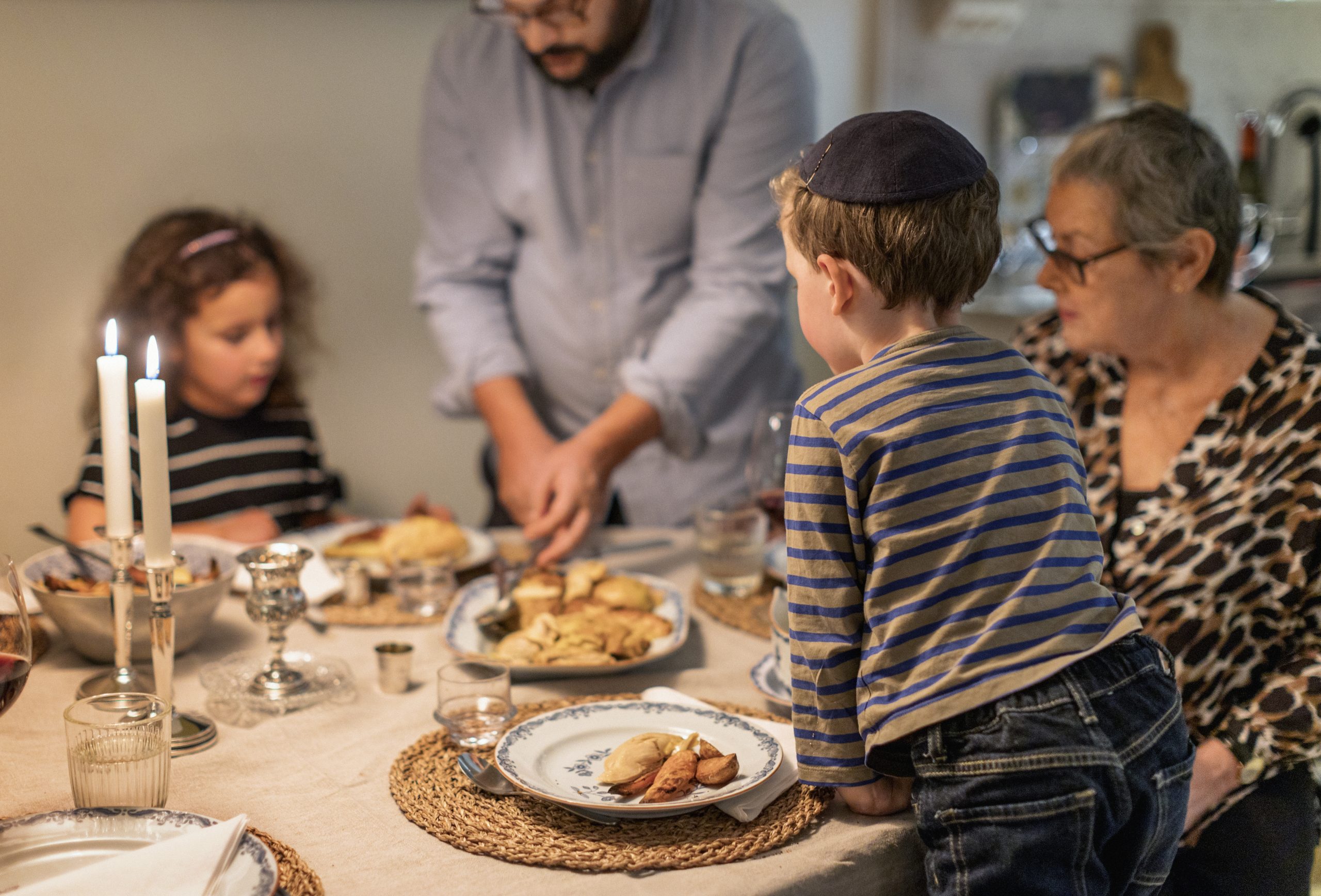 En familj sitter runt ett middagsbord. Ett barn har kippa på huvudet.