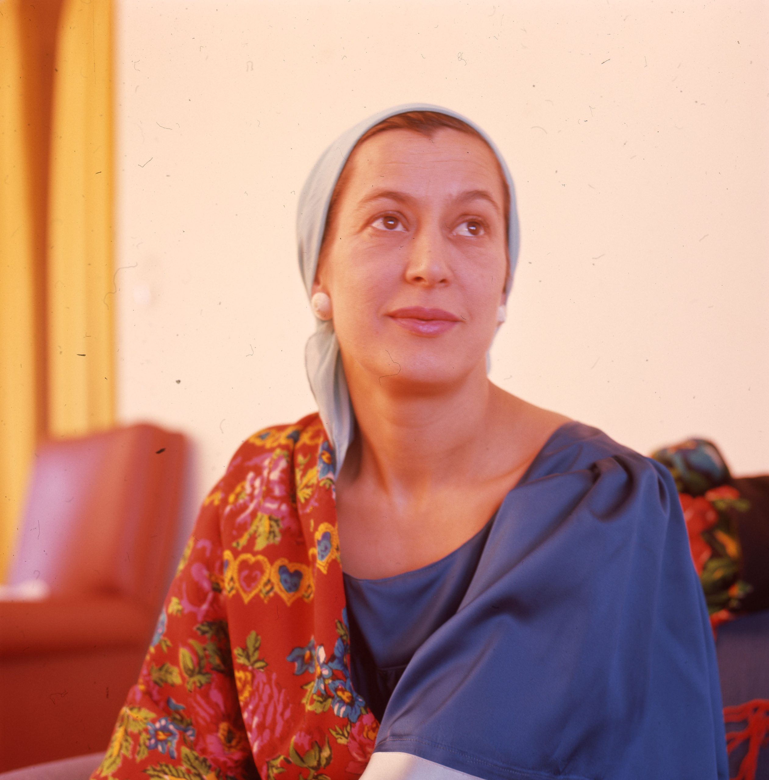 En ung kvinna med färgglada kläder och sjal över året blickar förbi kameran och ser ut att kanske fundera över något.