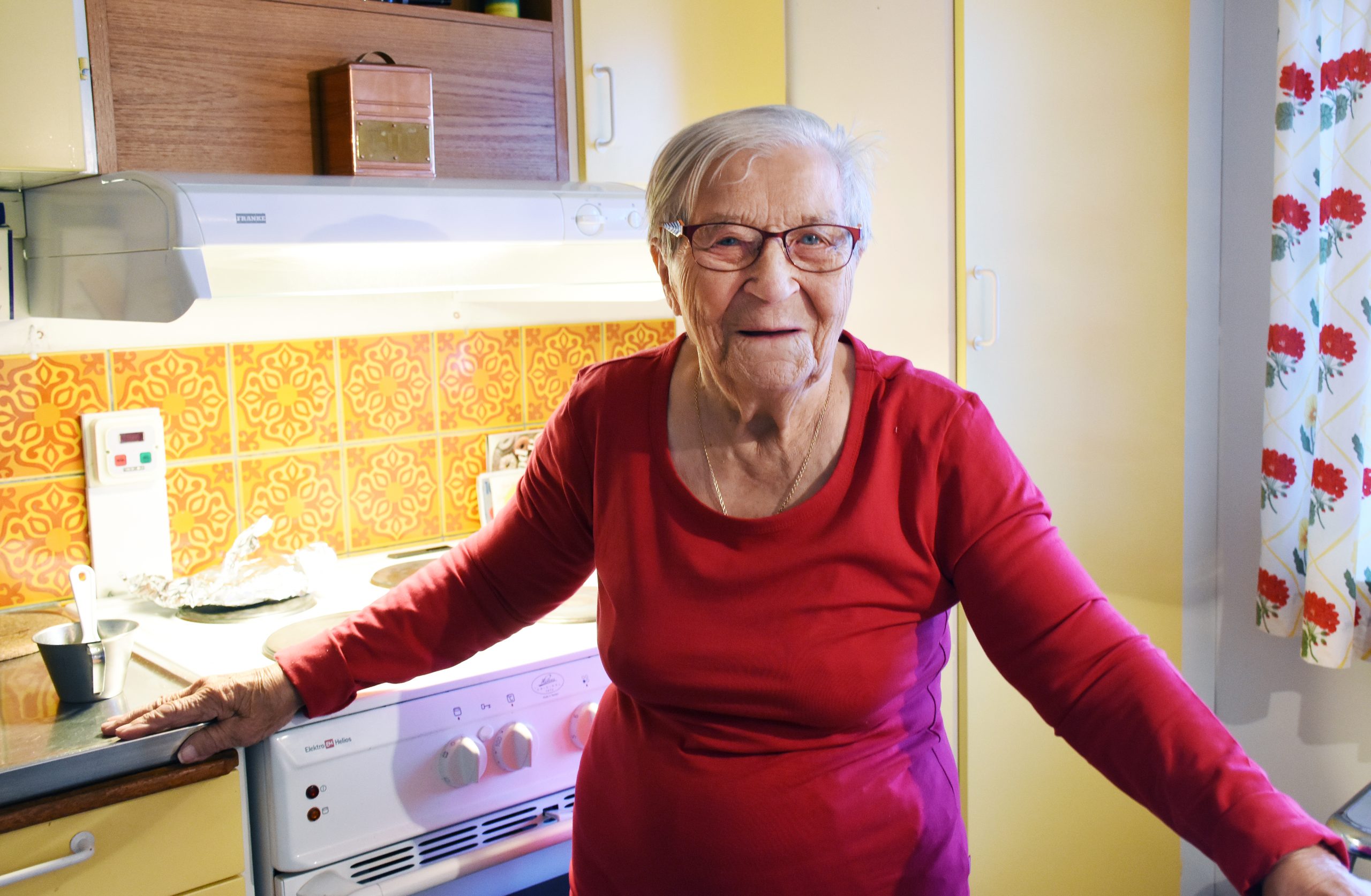 Susanna Huuva. En äldre kortklippt kvinna i röd tröja. Hon bär glasögon och ler mot kameran.