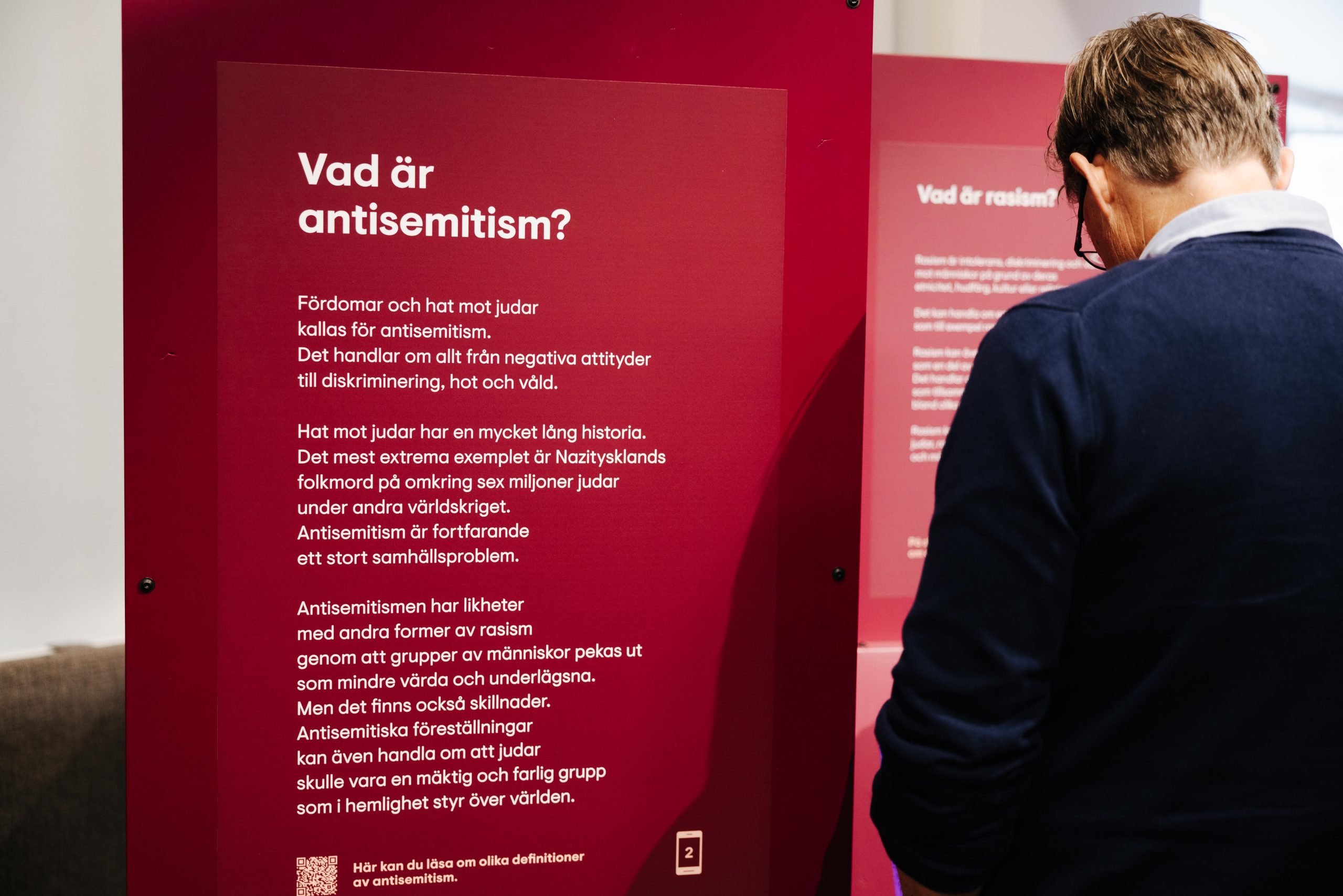 En person står i en utställning och läser en text på väggen som handlar om antisemtitism.
