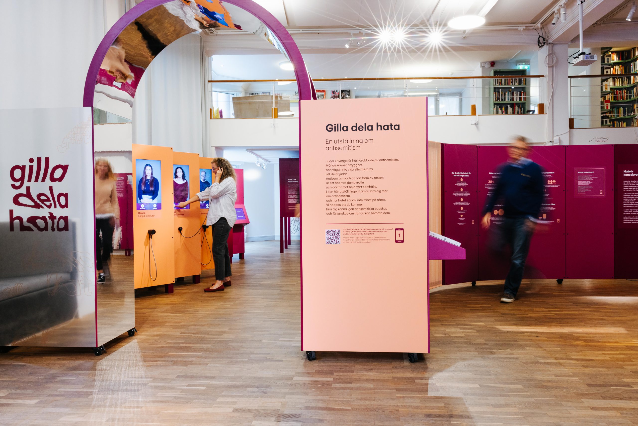 En utställningslokal med moduler i olika färger, med text och vude på, En kvinna syns i bakgrunden.