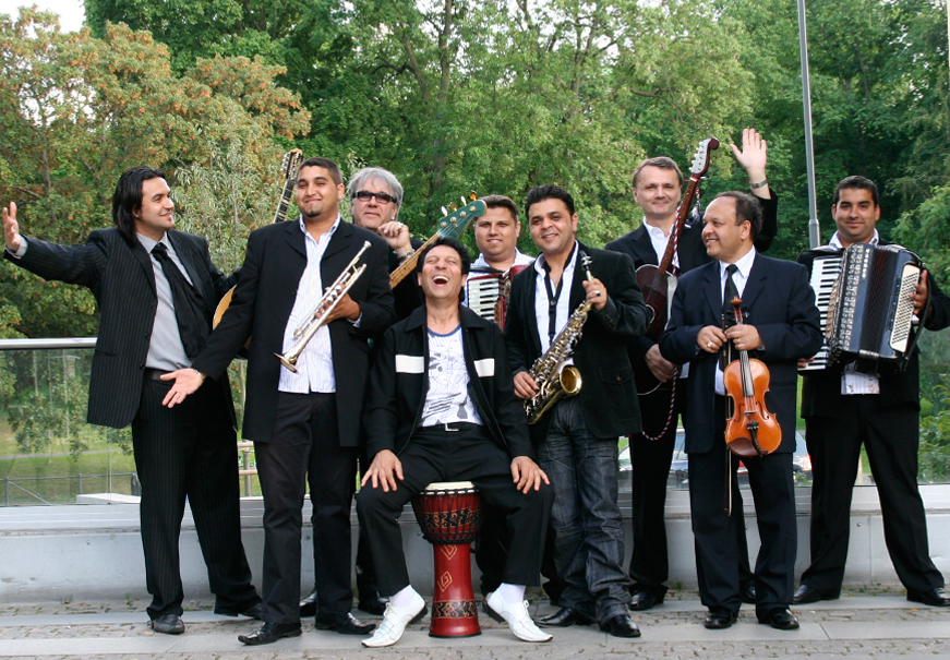 En gruppbild av nio musiker i svarta kostymer. De håller i instrument så som dragspel, saxofon och fiol.