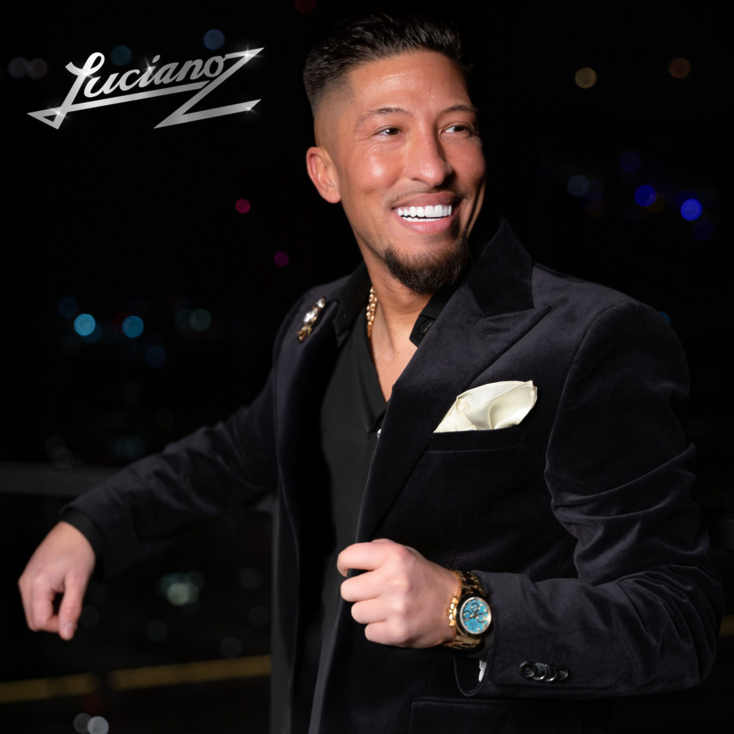 En ung man i kavaj blickar leende förbi kameran. Ovanpå builden står i silverglänsande text "Lucianoz".