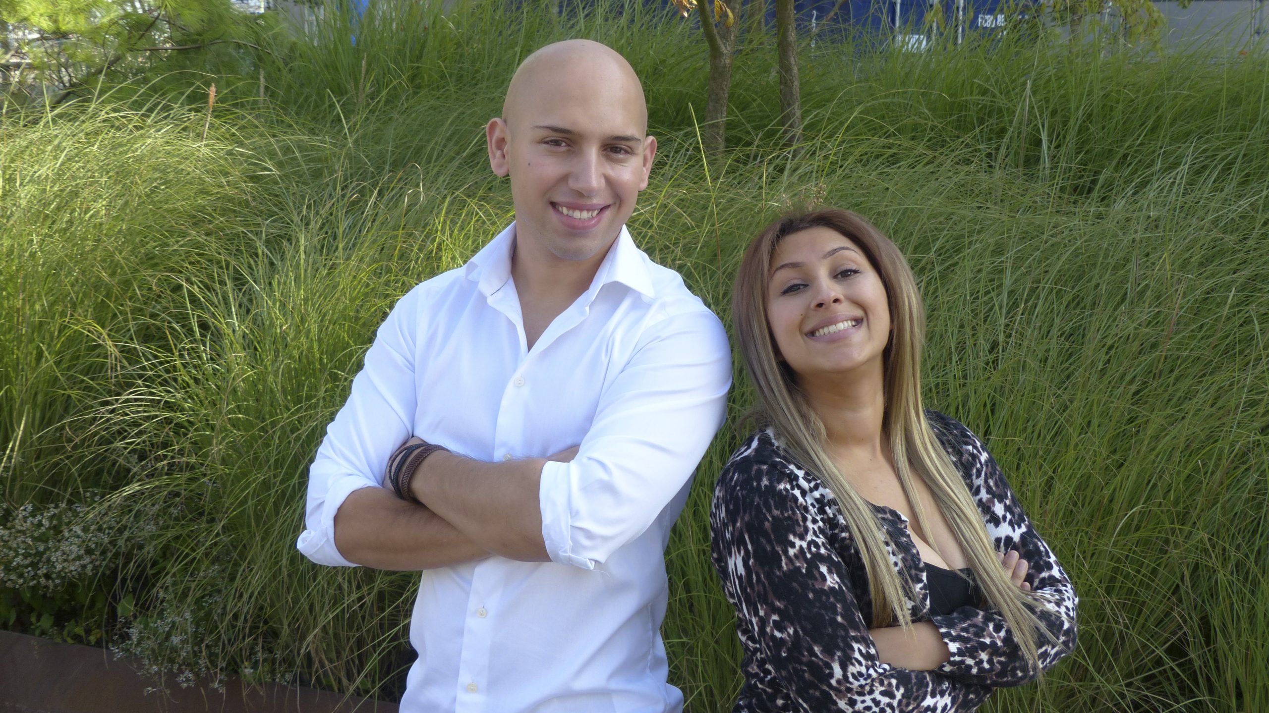 En ung kvinnao ch en ung man står rygg mot rygg på en sommaräng och blickar in i kameran.