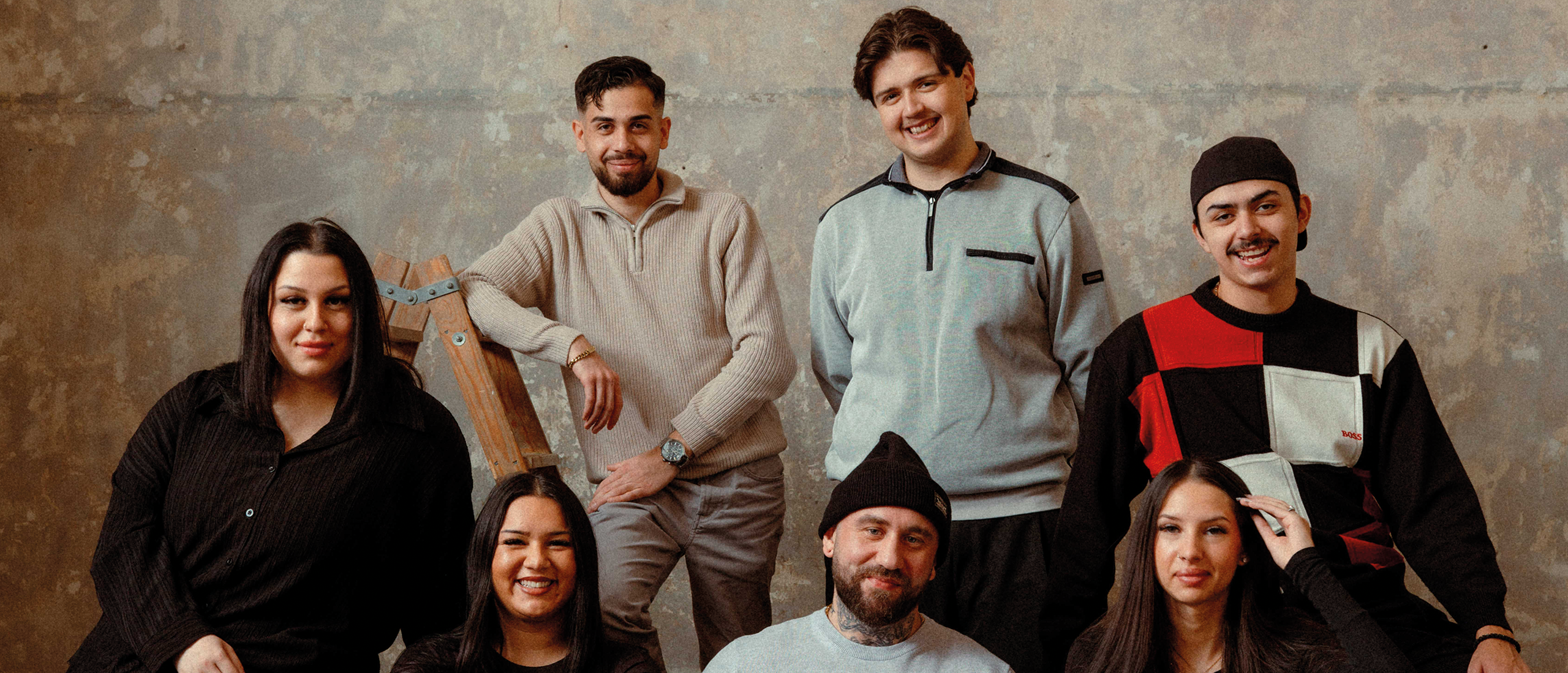 Sju personer står och sitter framför en vägg.