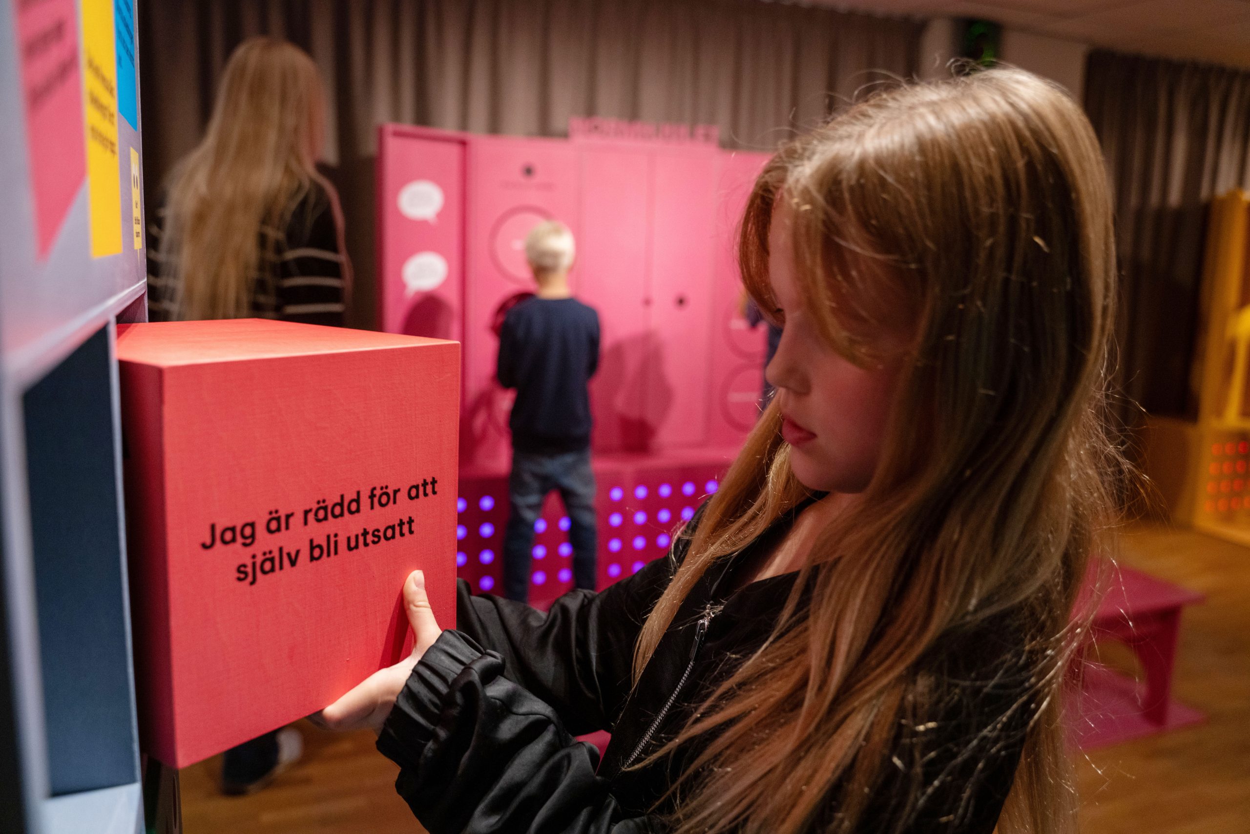 En flicka står vid en hylla och tittar på en röd box med texten "Jag är rädd för att själv bli utsatt"